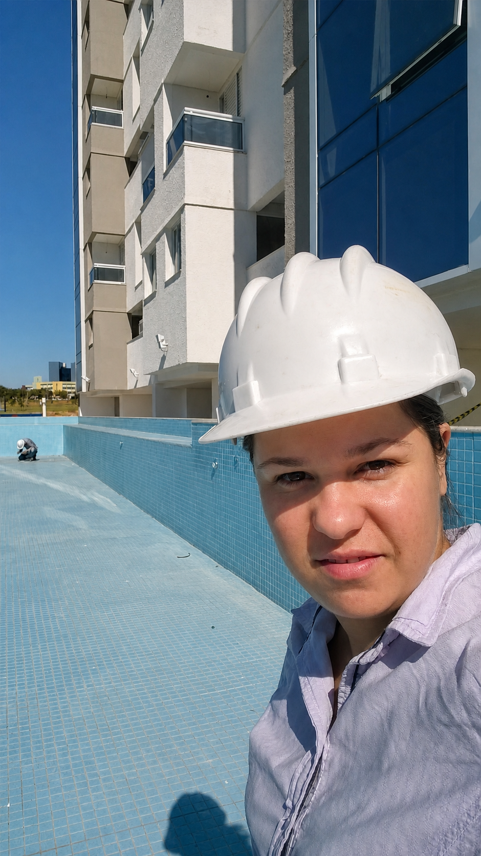Karine Gonçalves de capacete branco em obra, com piscina e edifício ao fundo